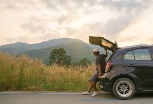 man leaning on car on road trip